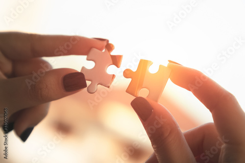 Hands of a woman hands holding two pieces of a puzzle in front of the sun with lens flare.