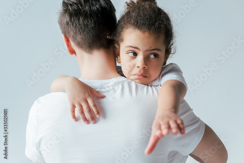 Canvas Print back view of foster father taking away sad african american daughter isolated on