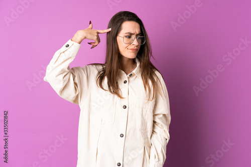 Young woman over isolated purple background making the gesture of madness putting finger on the head