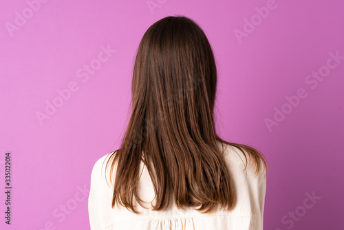 Young woman over isolated purple background in back position