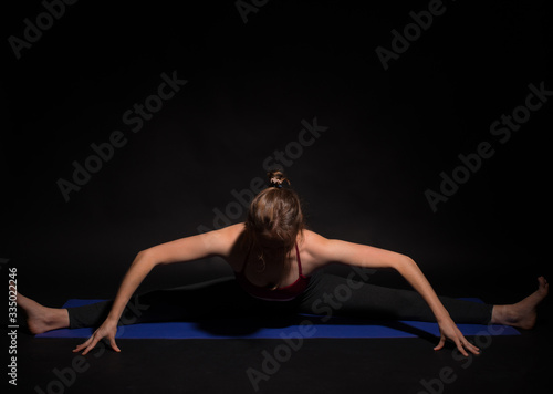 Photo of young sport woman doing yoga on mat over dark background