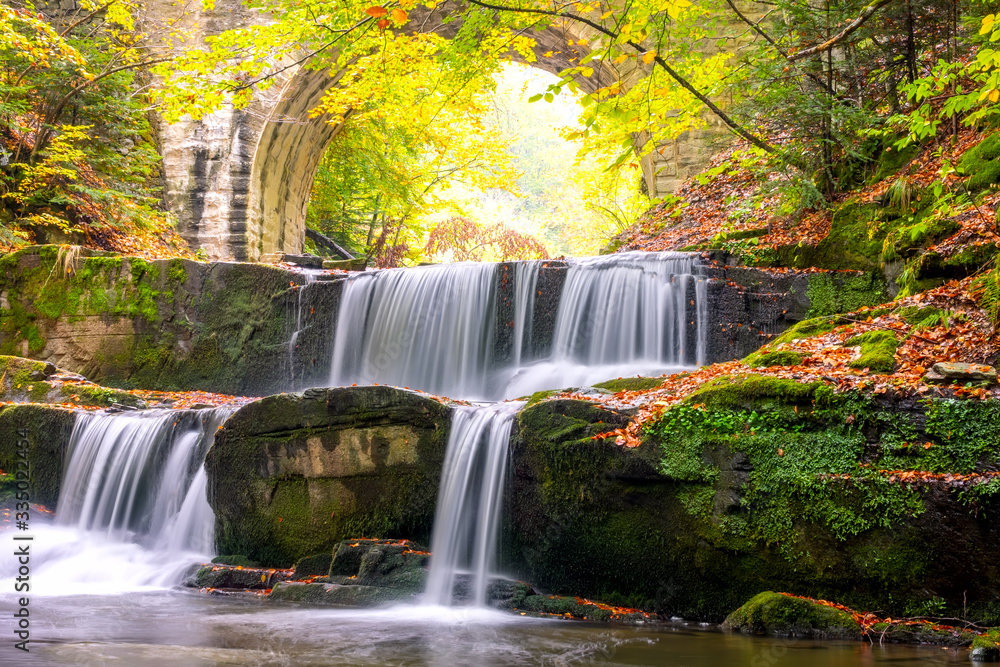 River Waterfall and Arch of a Stone Bridge in the Forest