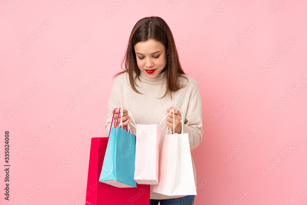 Teenager girl isolated on pink background holding shopping bags and looking inside it Teenager girl isolated on pink background holding shopping bags and looking inside it