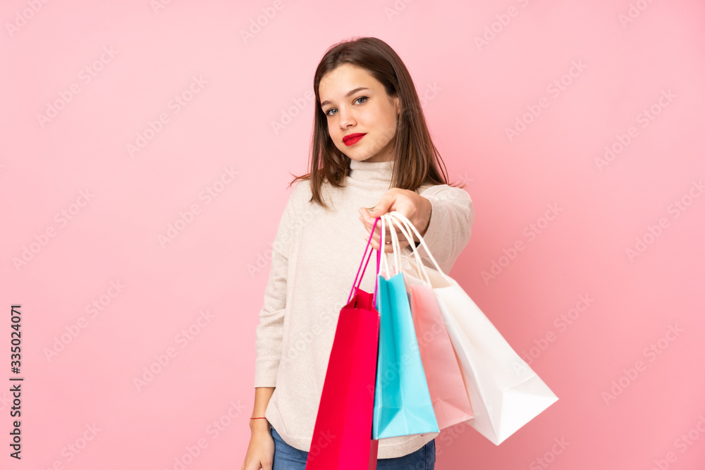Teenager girl isolated on pink background holding shopping bags and giving them to someone Teenager girl isolated on pink background holding shopping bags and giving them to someone