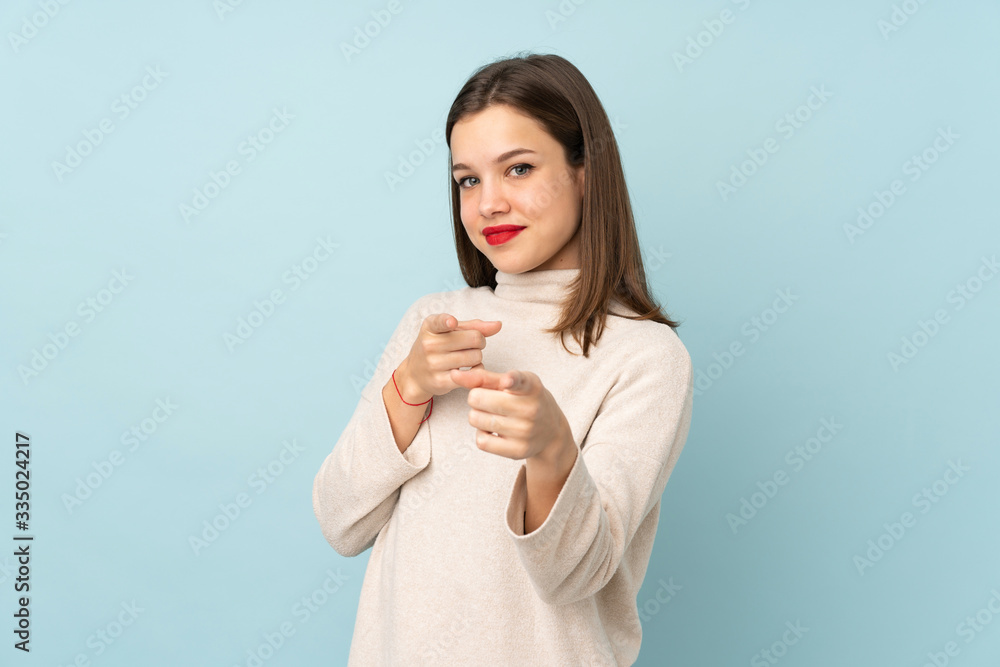 Teenager girl isolated on blue background points finger at you Teenager girl isolated on blue background points finger at you