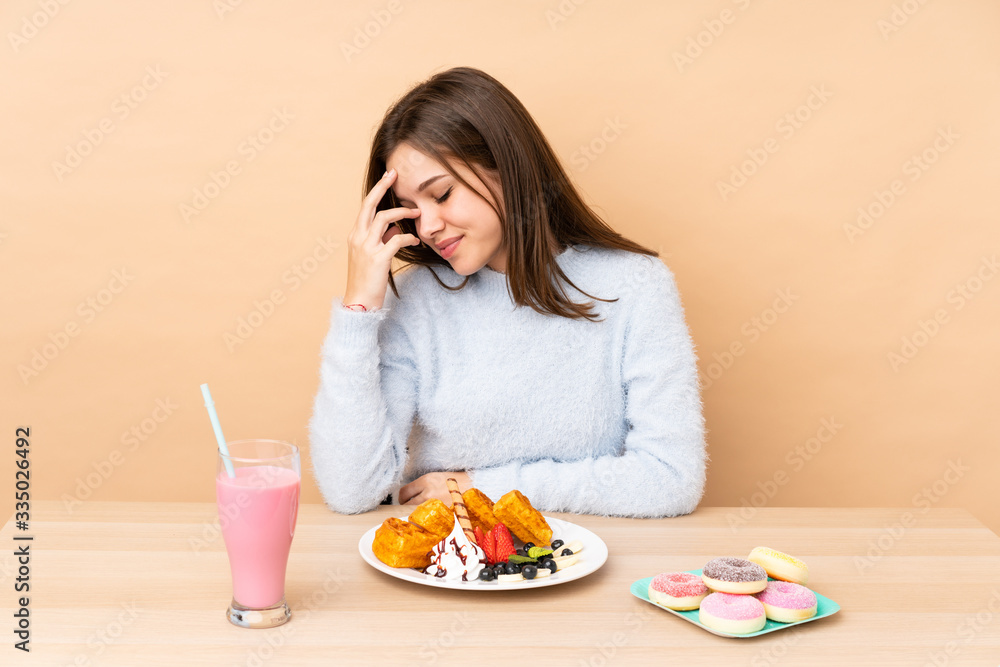 Teenager girl eating waffles isolated on beige background laughing Teenager girl eating waffles isolated on beige background laughing