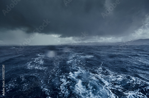The view of the stormy sea and mountains from the sailboat, Path from foam after the boat, splashes from under the boat, rainy weather, dramatic sky
