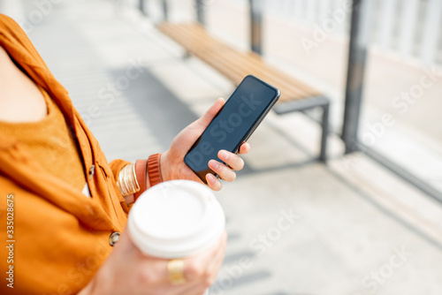 Business woman holding smart phone and coffee cup outdoors, close-up on hands, phone with black screen