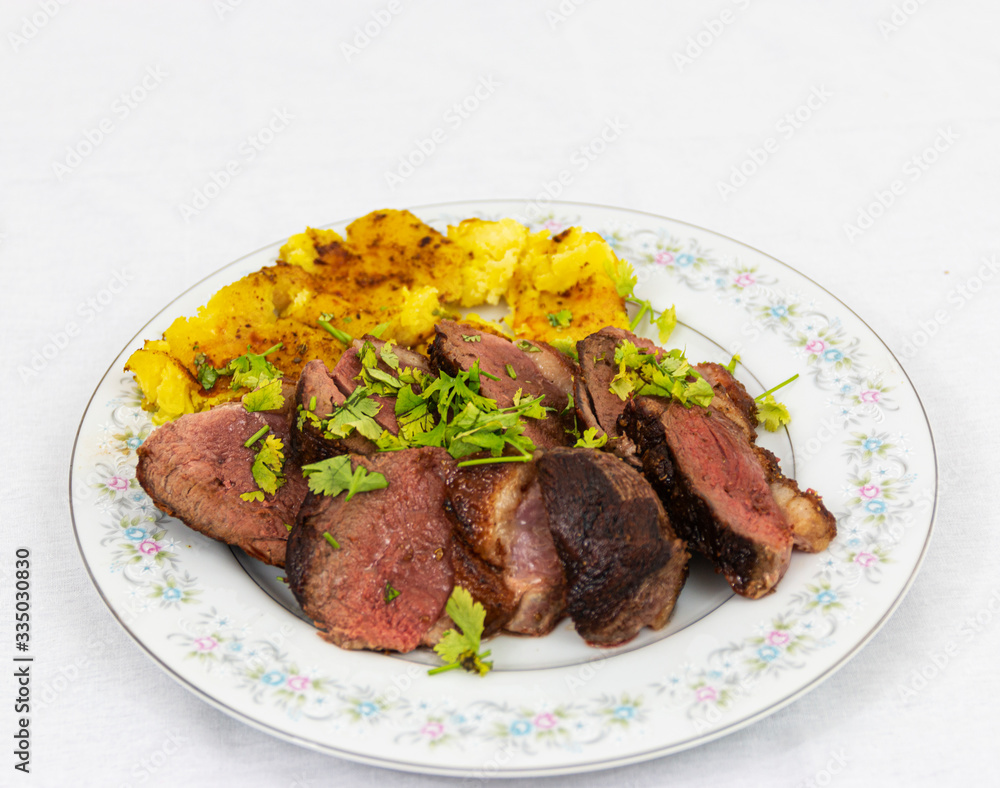 Sliced duck breast plated on a China plate with rosted potatos