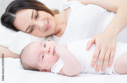 A young mother lies next to a newborn baby who lies on a large bed in the bedroom
