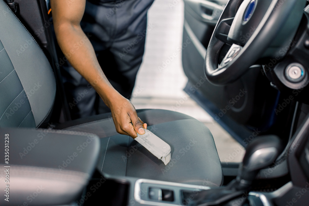 Hand of car service male dark skinned worker cleaning car seat with brush inside. Cleaning the car with brush, car detailing concept