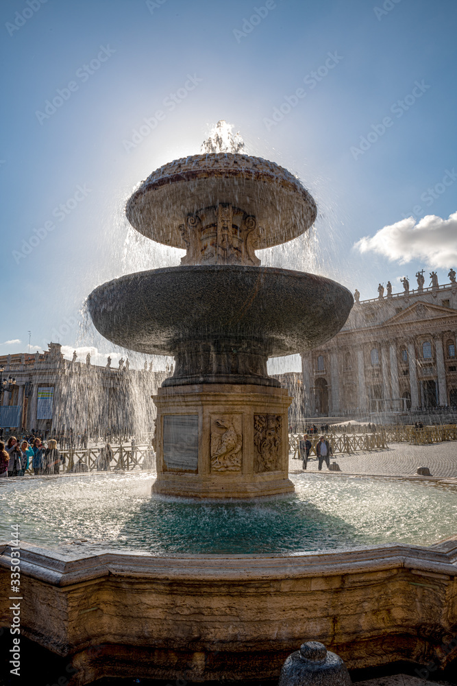 Zabytki na placu Św. Piotra w Watykanie. Na pierwszym planie ogromna fontanna, a w oddali widać bazylikę świętego Piotra, Włochy. - obrazy, fototapety, plakaty 