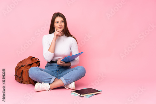 Teenager caucasian student girl sitting on the floor isolated on pink background thinking an idea while looking up