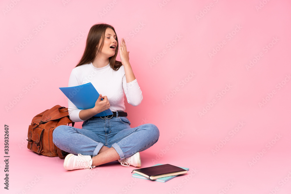 Teenager caucasian student girl sitting on the floor isolated on pink background yawning and covering wide open mouth with hand Teenager caucasian student girl sitting on the floor isolated on pink background yawning and covering wide open mouth with hand
