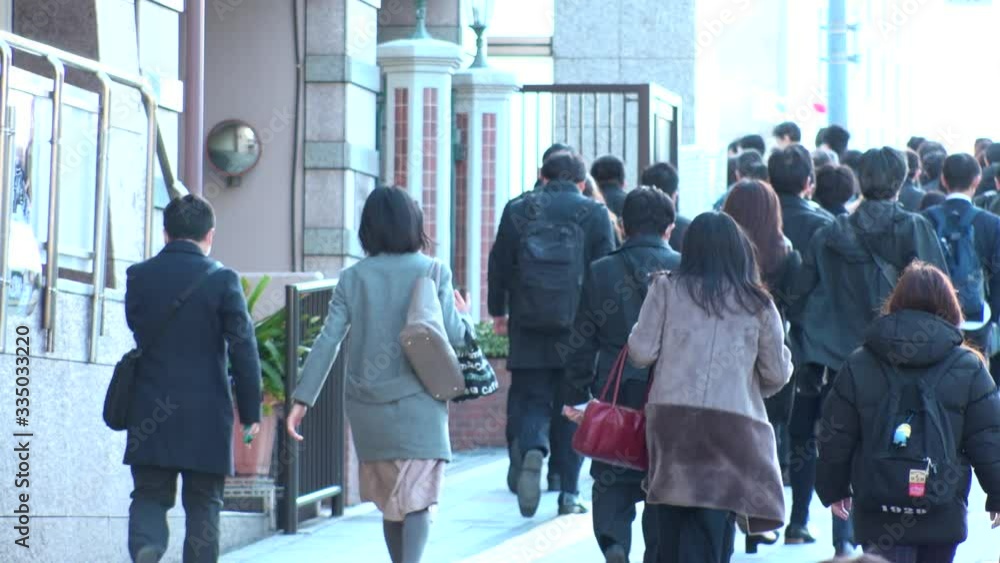 TOKYO, JAPAN - MARCH 2020 : View of crowd of people walking down the street in busy morning rush hour. Many commuters going to work. Japanese business, job and lifestyle concept. Slow motion shot. TOKYO, JAPAN - MARCH 2020 : View of crowd of people walking down the street in busy morning rush hour. Many commuters going to work. Japanese business, job and lifestyle concept. Slow motion shot.