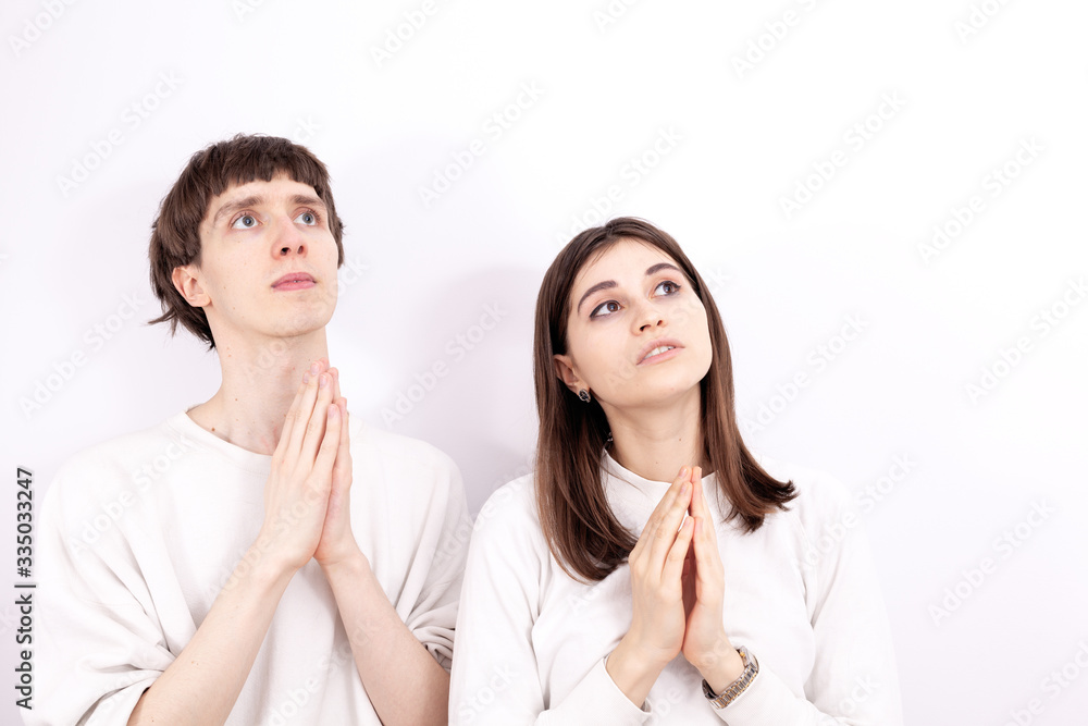 The young couple in a white sweatshirts are looking at the sky. They are praying and keeps their hands folded in the pray. The young girl stands next to him. The young couple in a white sweatshirts are looking at the sky. They are praying and keeps their hands folded in the pray. The young girl stands next to him.