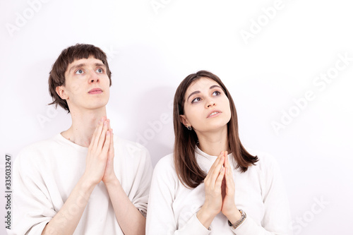 The young couple in a white sweatshirts are looking at the sky. They are praying and keeps their hands folded in the pray. The young girl stands next to him.