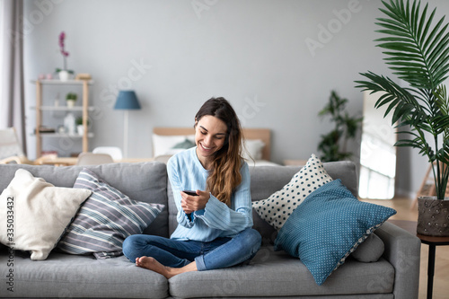 Online chat. Smiling woman talking on smartphone with friends while sitting on sofa at home.