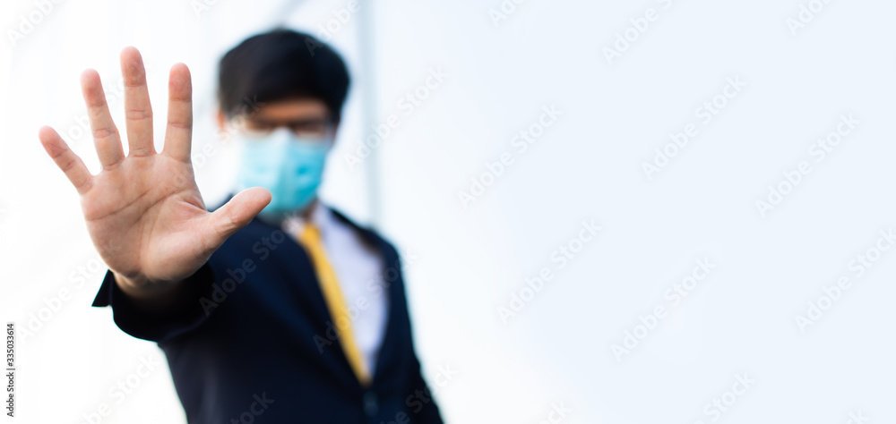 Young Asian business man in protective sterile medical mask on face looking at camera showing gesture stop, stop no sign. People in masks outbreak of Corona virus (2019-nCoV)