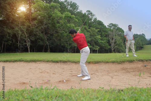 Golfer hitting the ball on the sand.