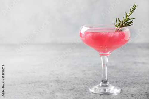 Glass of sparkling rose wine with shimmer edible glitter garnish rosemary on grey.