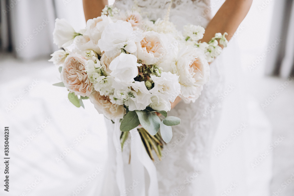 young girl in a white wedding dress holds in her hands a bouquet of flowers and greenery with a ribbon