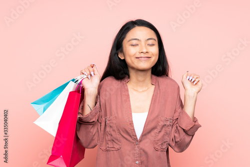 Teenager Chinese girl isolated on pink background holding shopping bags and smiling