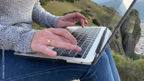 Woman typing keyboard laptop at Meteora Mountains at sunset. Close up of hands typing text at laptop keyboard outdoor.
