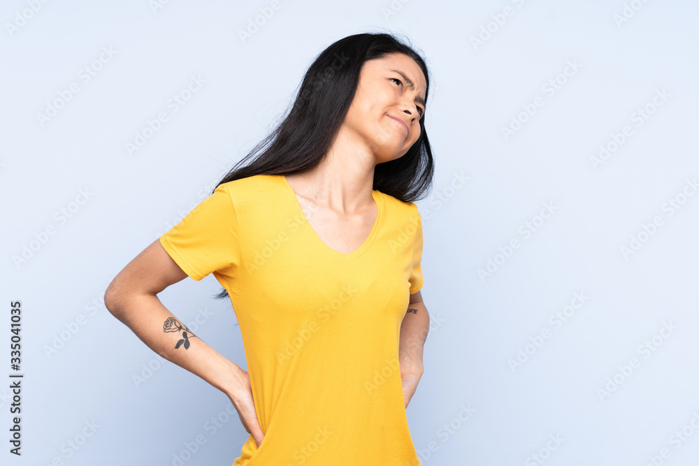 Teenager Chinese woman isolated on blue background suffering from backache for having made an effort Teenager Chinese woman isolated on blue background suffering from backache for having made an effort