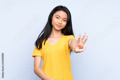 Teenager Chinese woman isolated on blue background happy and counting three with fingers