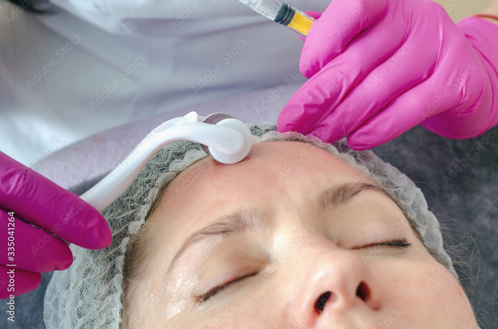 Cosmetologist performs a facial massage using a mesoscooter. Wom Cosmetologist performs a facial massage using a mesoscooter. Wom