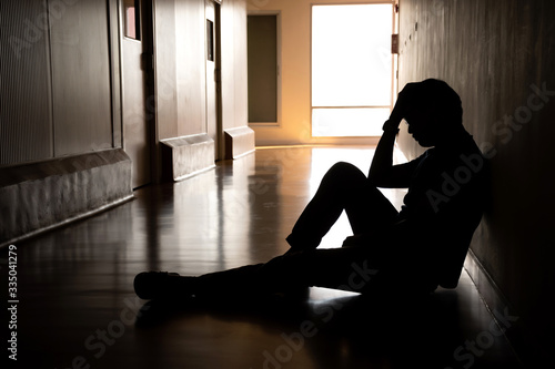 Silhouette of depressed man sitting on walkway of residence building. Sad man, Cry, drama, lonely and unhappy concept.