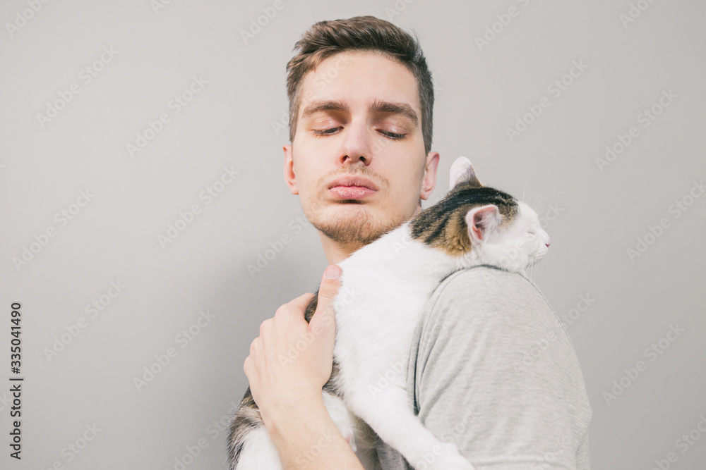 Young man with cute funny cat on light background Young man with cute funny cat on light background