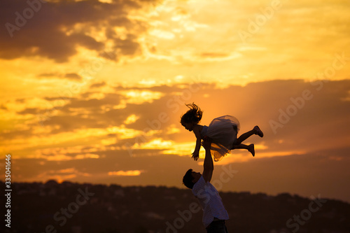 silhouette of dad throws daughter at sunset.