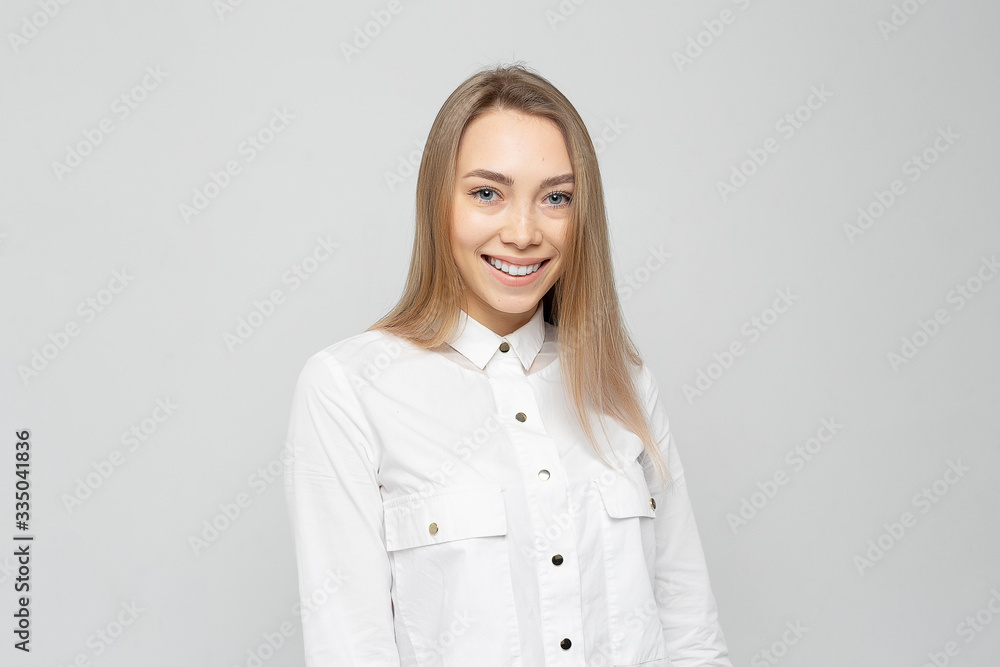 Beautiful young woman portrait. Portrait of a beautiful smiling blonde girl in a white shirt on a white-gray Beautiful young woman portrait. Portrait of a beautiful smiling blonde girl in a white shirt on a white-gray