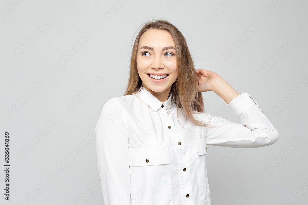 Beautiful young woman portrait. Portrait of a beautiful smiling blonde in white shirt on a white-gray. woman straightens her hair or holds her head Beautiful young woman portrait. Portrait of a beautiful smiling blonde in white shirt on a white-gray. woman straightens her hair or holds her head