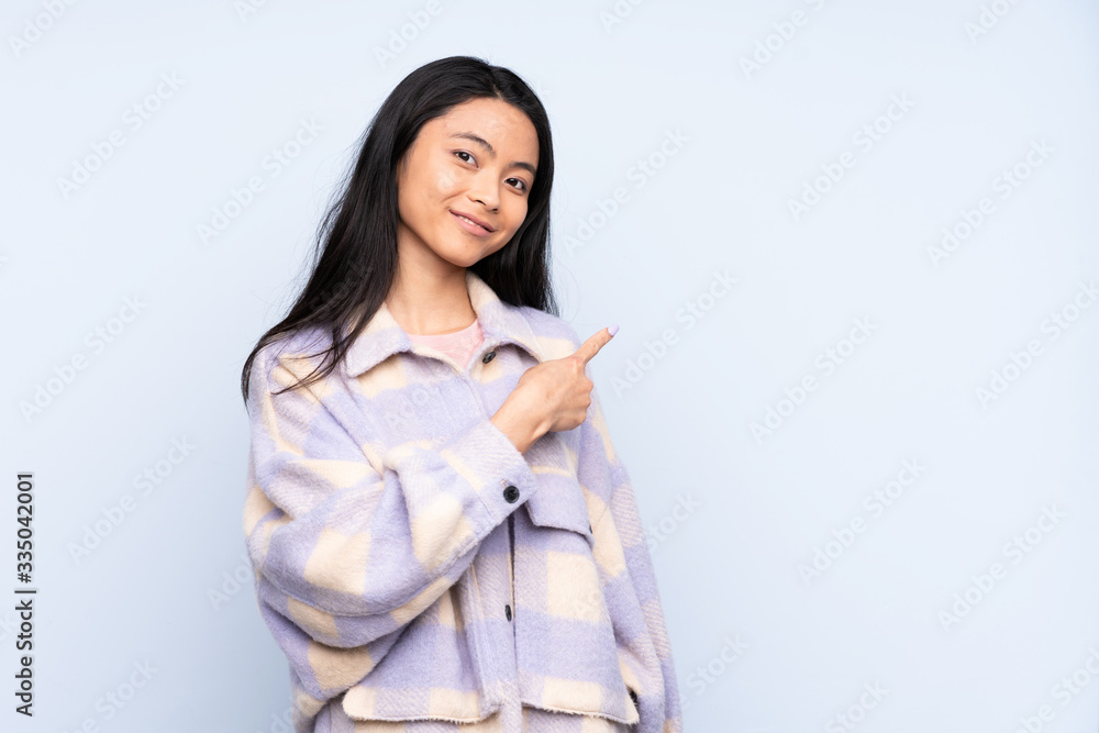 Teenager Chinese woman isolated on blue background pointing to the side to present a product Teenager Chinese woman isolated on blue background pointing to the side to present a product