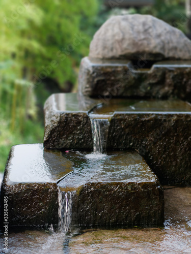 Beautiful three-tiered stone waterfall. Water flowing over rocks. Zen style garden fountain image.  Focused on foreground.