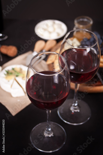 glasses of red wine and plate with assorted cheese, fruit and other snacks for party