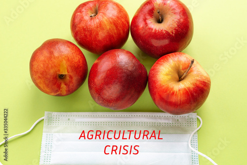 juicy apples in a protective medical mask with the inscription Agricultural crisis on a green background. Concept of harvest and economic crisis during the COVID-19 virus pandemic