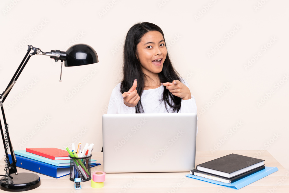 Student asian girl in a workplace with a laptop isolated on beige background pointing to the front and smiling Student asian girl in a workplace with a laptop isolated on beige background pointing to the front and smiling