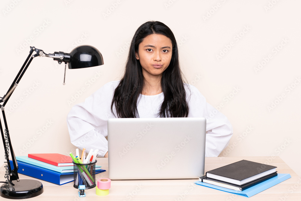 Student asian girl in a workplace with a laptop isolated on beige background angry Student asian girl in a workplace with a laptop isolated on beige background angry