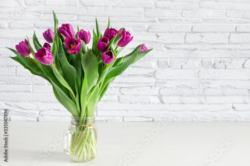 Fototapeta Naklejka Na Ścianę i Meble -  Beautiful purple tulip flowers bouquet on white shelf in front of white brick wall.