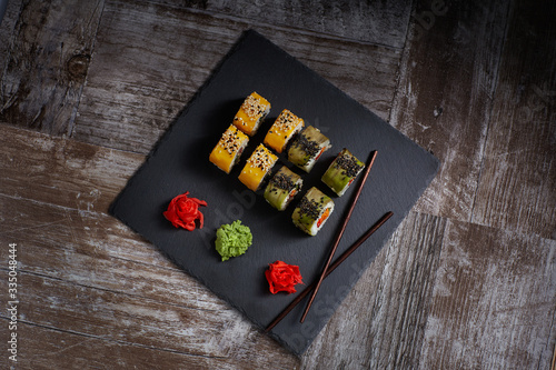 Sushi set on a square black plate of stone. Ginger and chopsticks are next to the set.  Top view . Old Wood Background