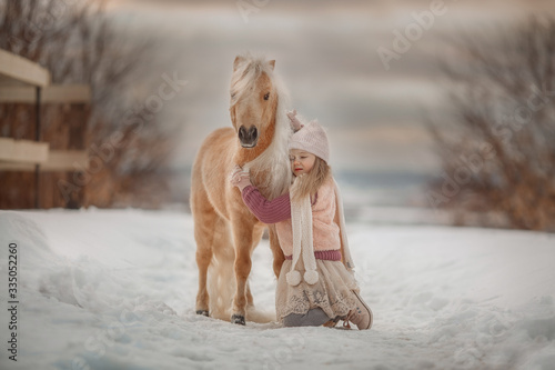 Fotografie Little girl with palomino miniature horse in winter park