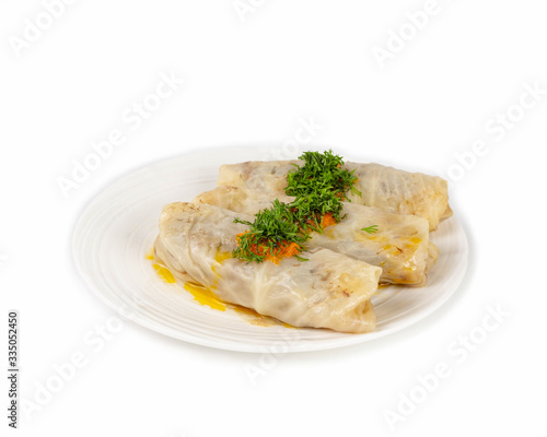 Cabbage rolls in a white plate sprinkled with chopped fresh dill on a white background