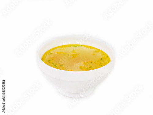 Bowl of golden broth with chopped herbs on a white background side view