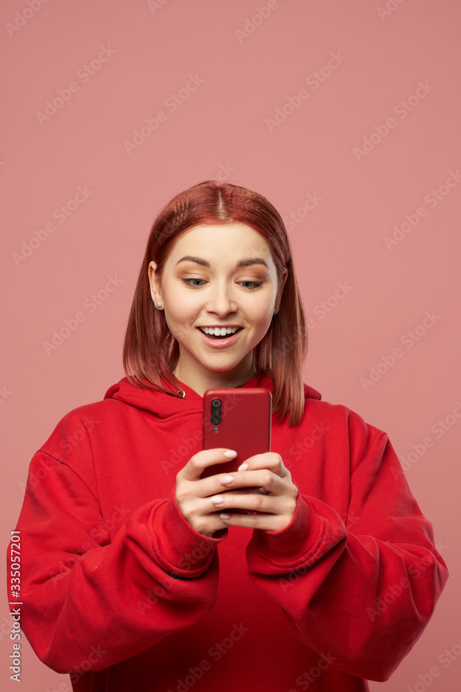 Smiling ginger woman with phone in her hands standing in studio Smiling ginger woman with phone in her hands standing in studio