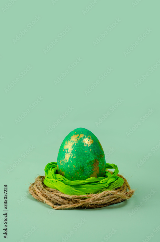 Easter egg in decorative nest  on turquoise background. Minimalism concept. Happy Easter background. 
