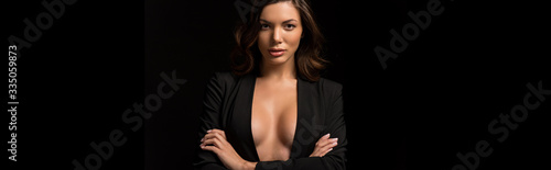 panoramic shot of confident, seductive girl in unbuttoned blazer posing with crossed arms isolated on black